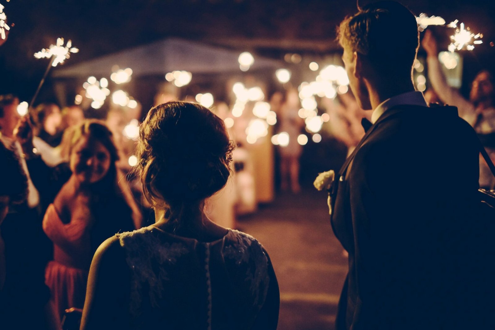 Couple walking through a reception lit by string lights at night