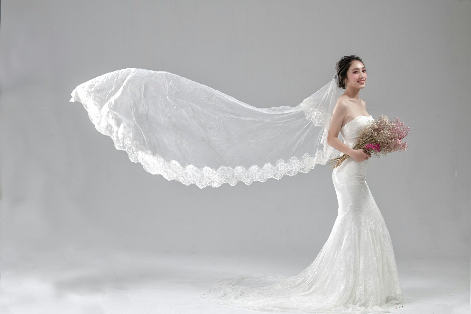 Bride holding a bouquet as her veil catches the wind